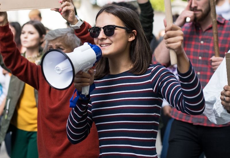 Jente som holder megafon og plakat. Foto: Colourbox.