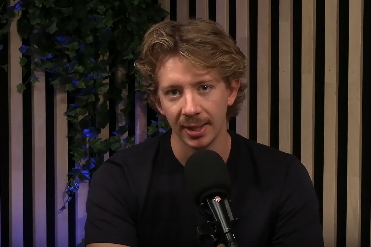 Komiker Henrik Schatvet ser rett i kamera mens han sitter i et podcast-studio.