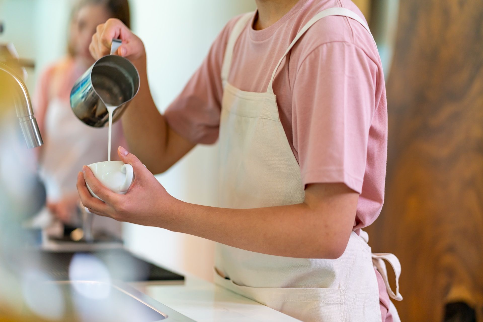 Foto av ung barista som heller varm melk i en kaffekopp.