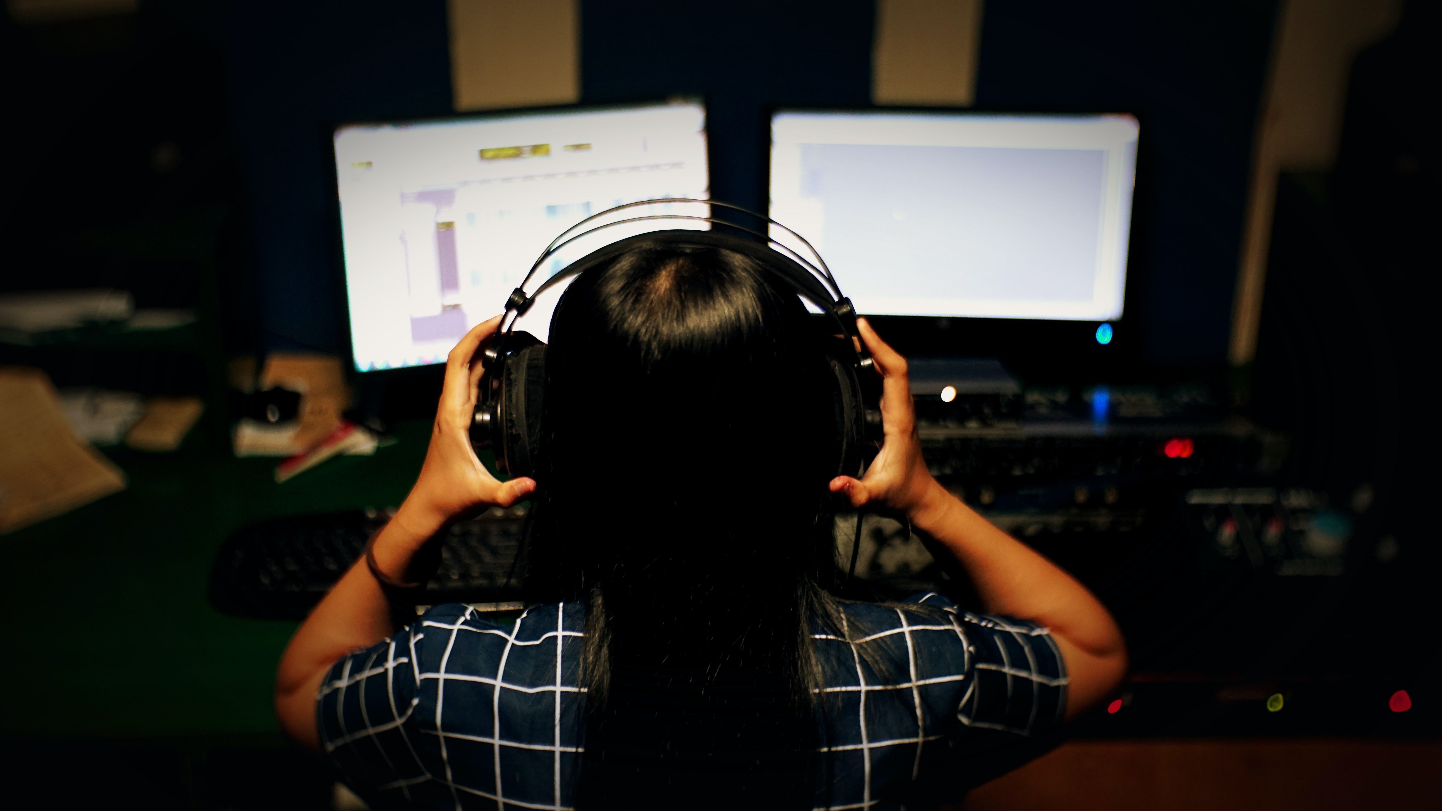 Ung jente som holder på headsettet mens hun sitter foran to pc-skjermer