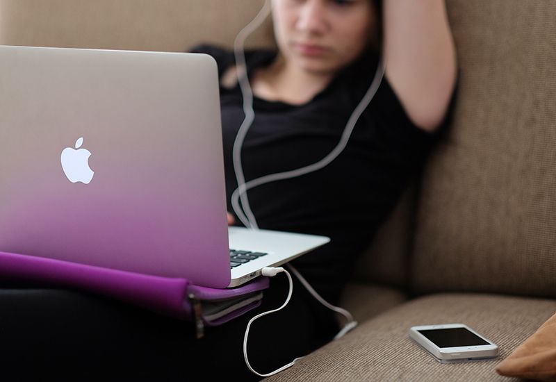 Jente sitter på sofaen med laptop og mobil (Foto: Steinar Engeland på Unsplash.com)