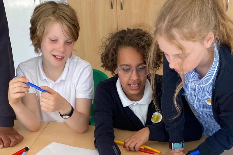Three older pupils working together at a table, drawing and talking.