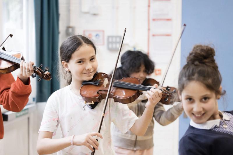 Primary school children playing violins together in a school hall.