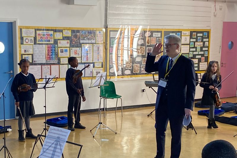 A composer conducting a small group of primary school children playing in a classroom.