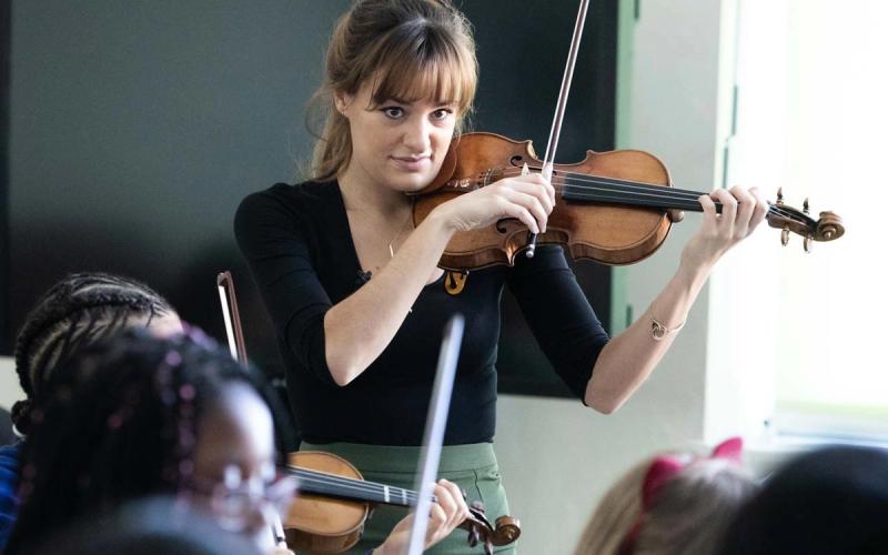 Violinist Nicola Benedetti playing alongside a Music Masters pupil in a school classroom.