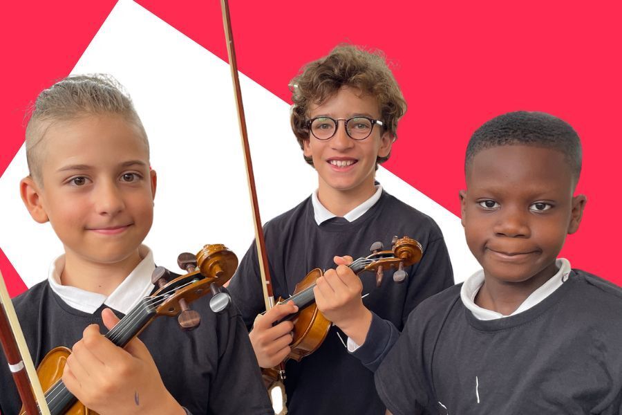 Three smiling schoolchildren in dark school jumpers holding violins and bows, against a red and white background.