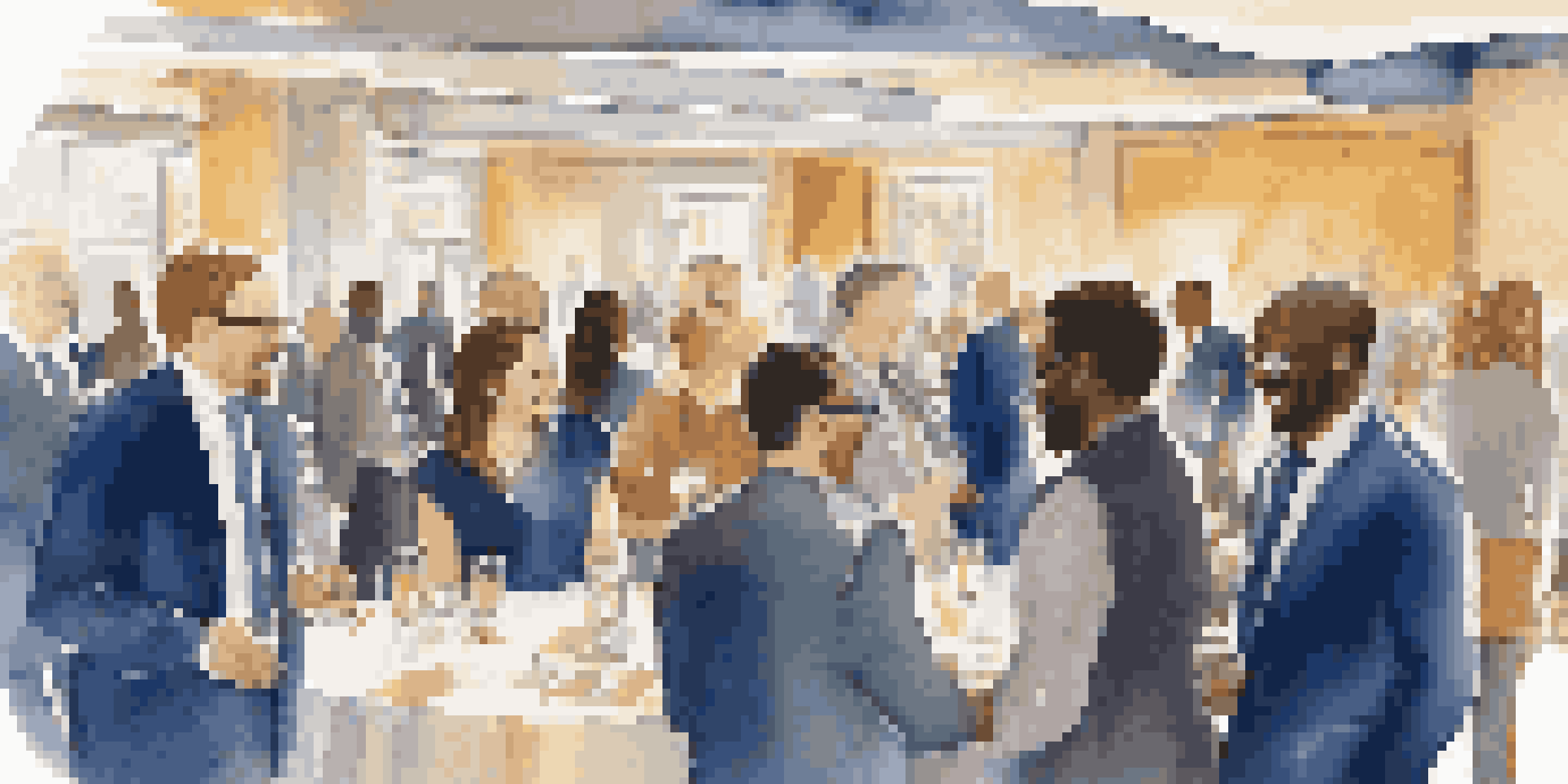 A diverse group of professionals networking at an event, smiling and shaking hands in a warmly lit room.