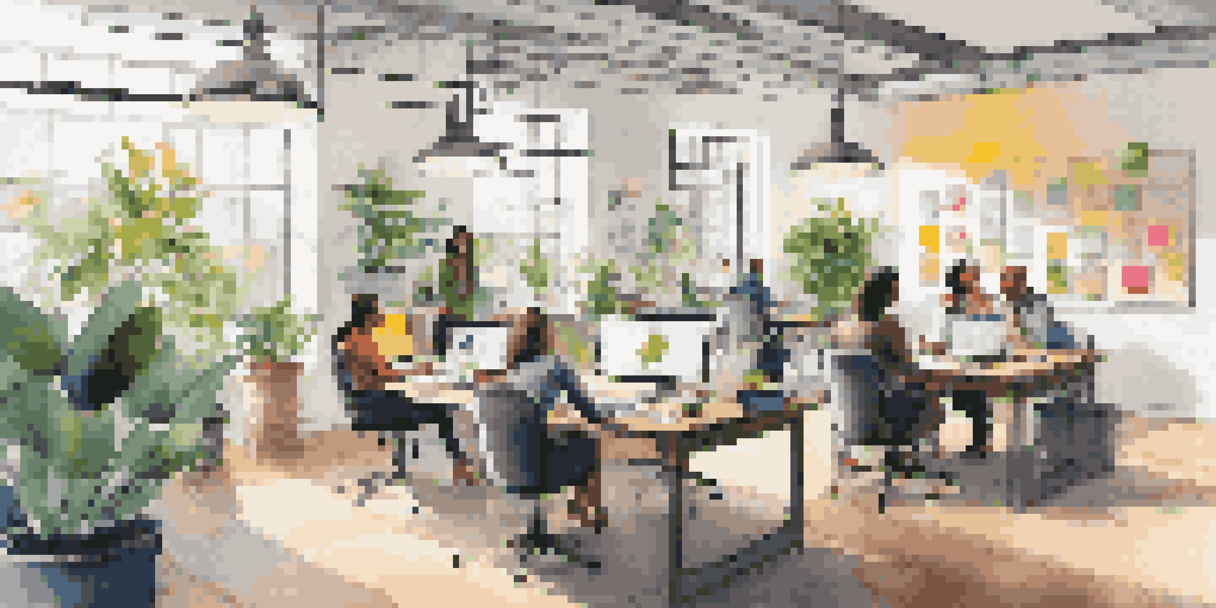 A modern workspace with diverse professionals collaborating at a table filled with laptops and notebooks, illuminated by natural light from large windows.