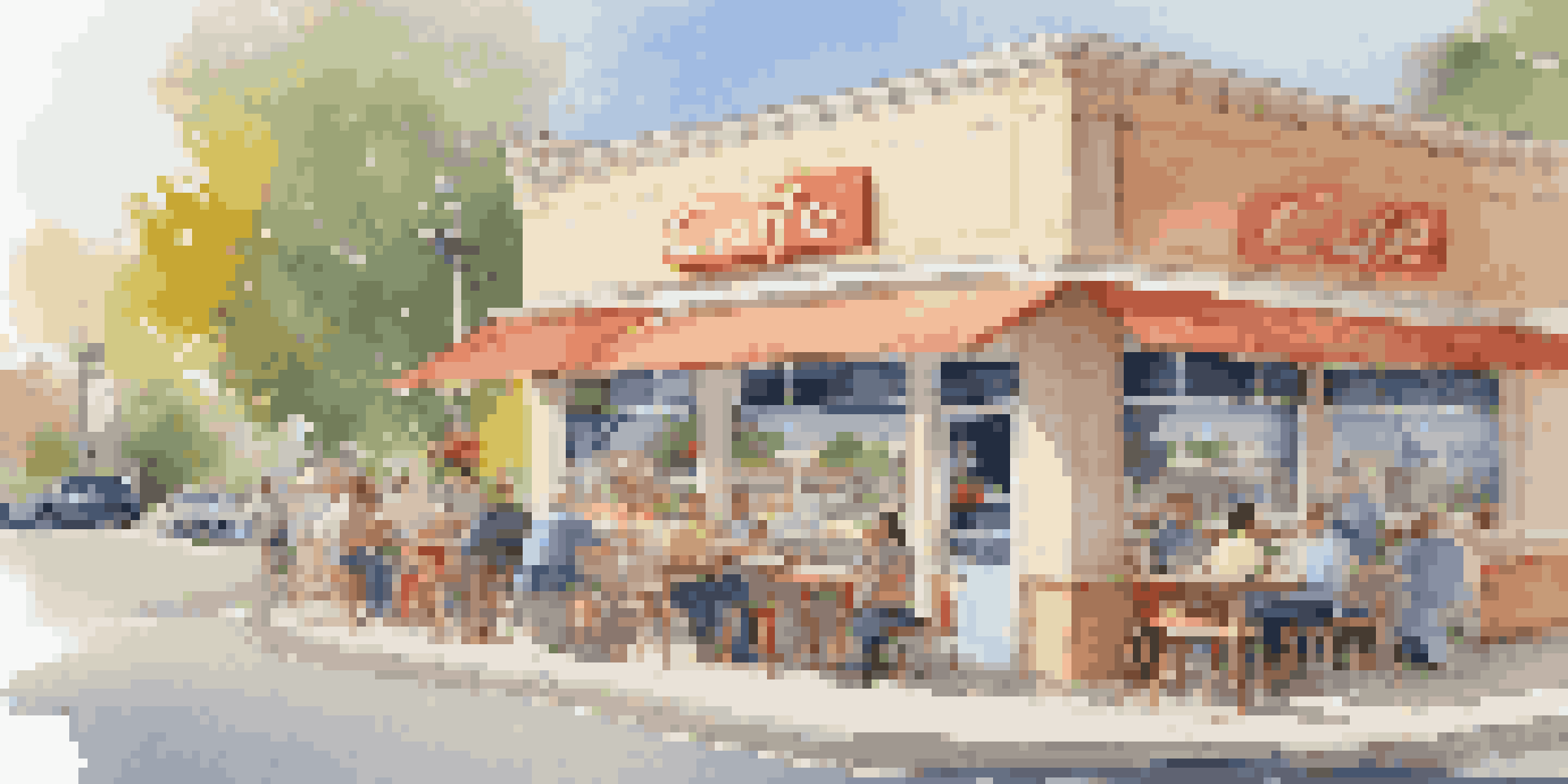 A busy café with a drive-thru service on a sunny day, people interacting at the window and others sitting outside.