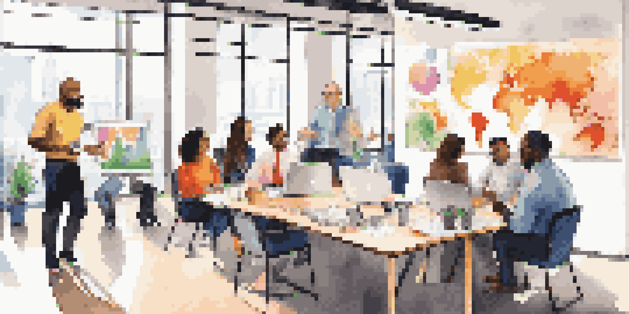 A diverse group of marketing team members gathered in a bright office, engaged in discussion with laptops and charts around them.