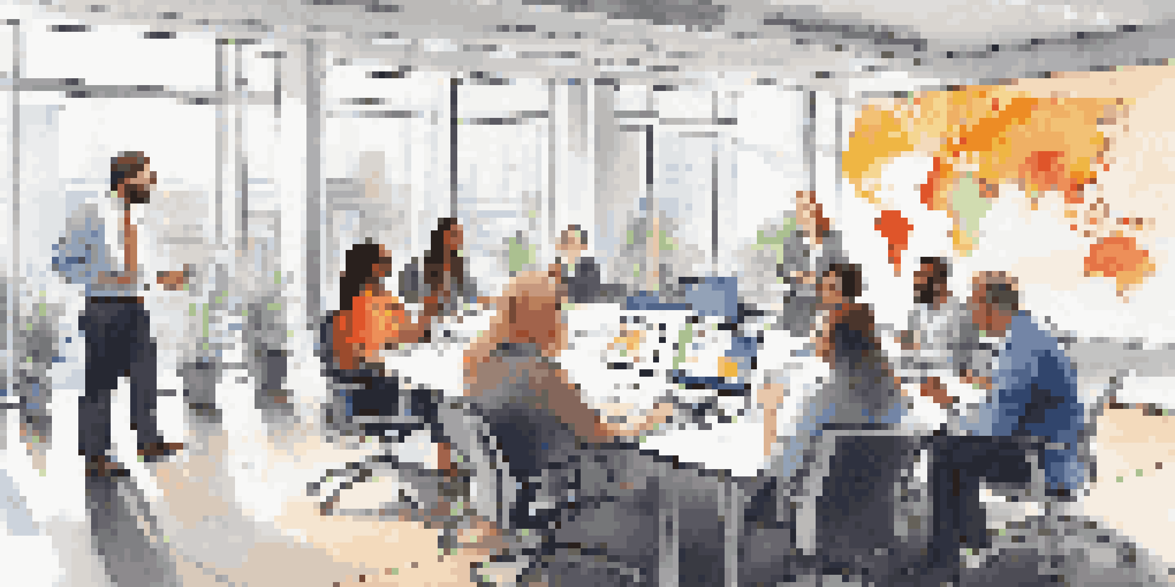 A diverse group of employees collaborating in a bright office meeting, with laptops and a whiteboard filled with notes.