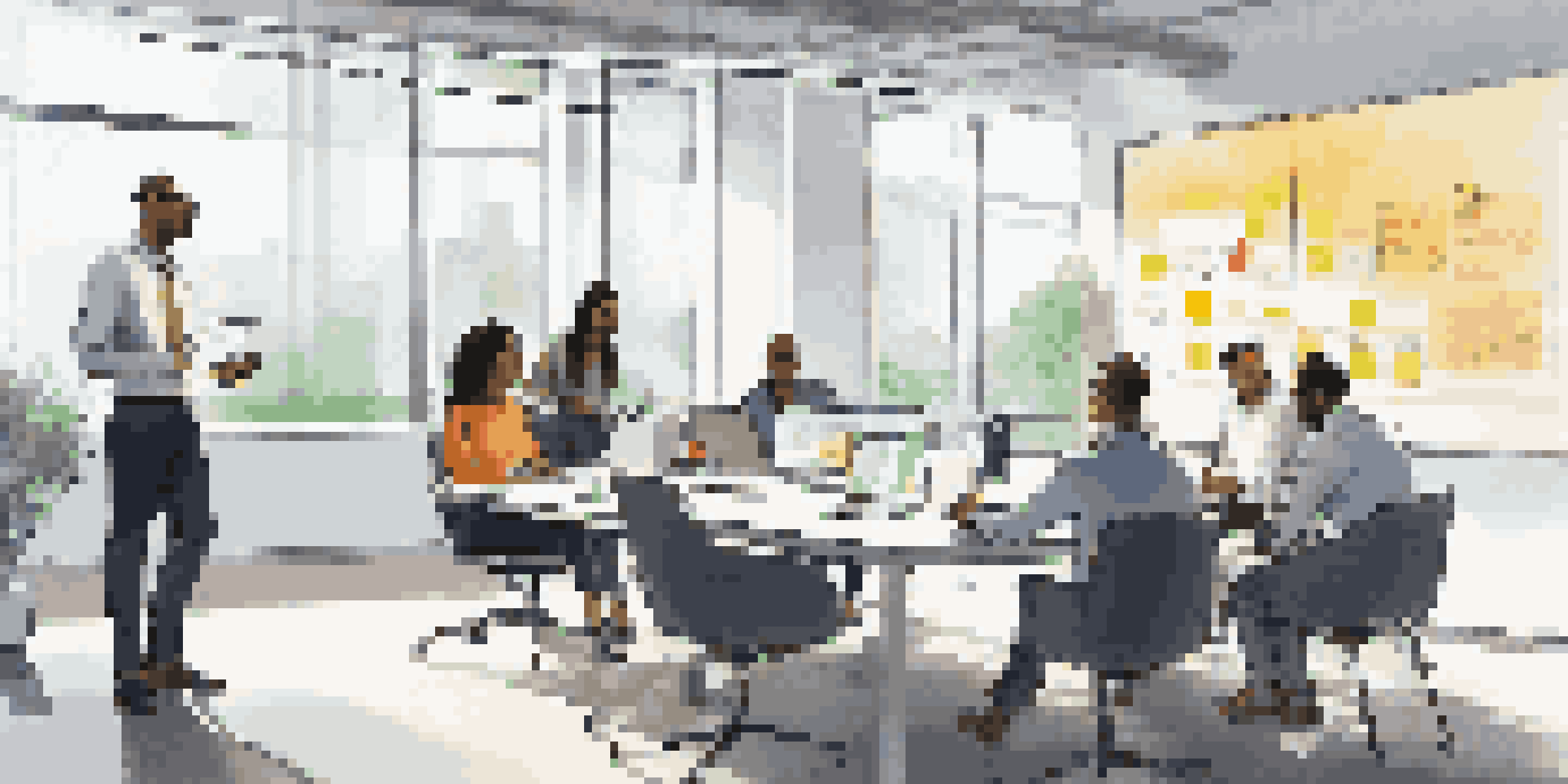 A diverse group of employees collaborating in a bright conference room with laptops and sticky notes.