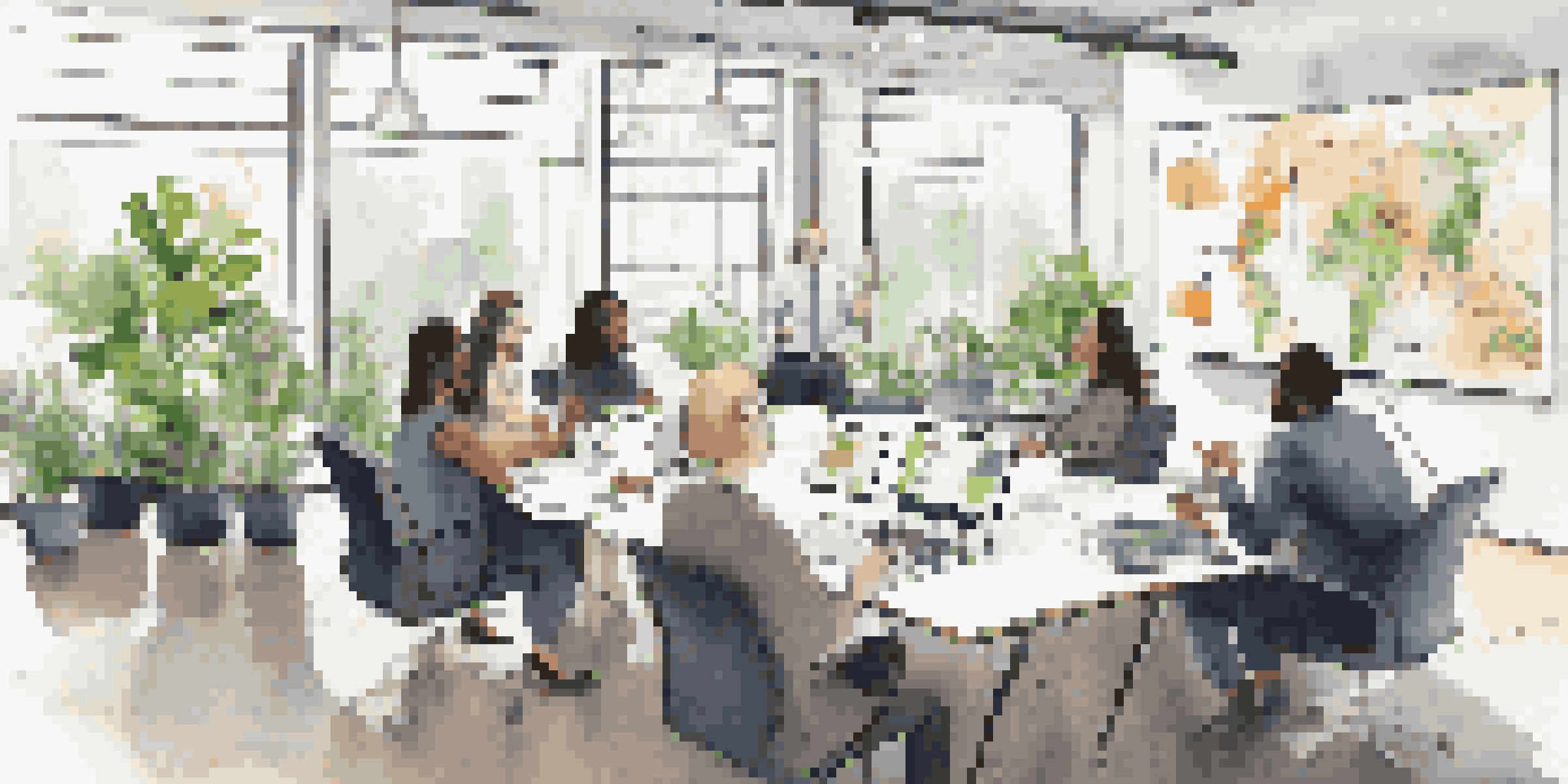 A diverse group of professionals engaged in a meeting with laptops and notepads, discussing business continuity planning with graphs on a screen.