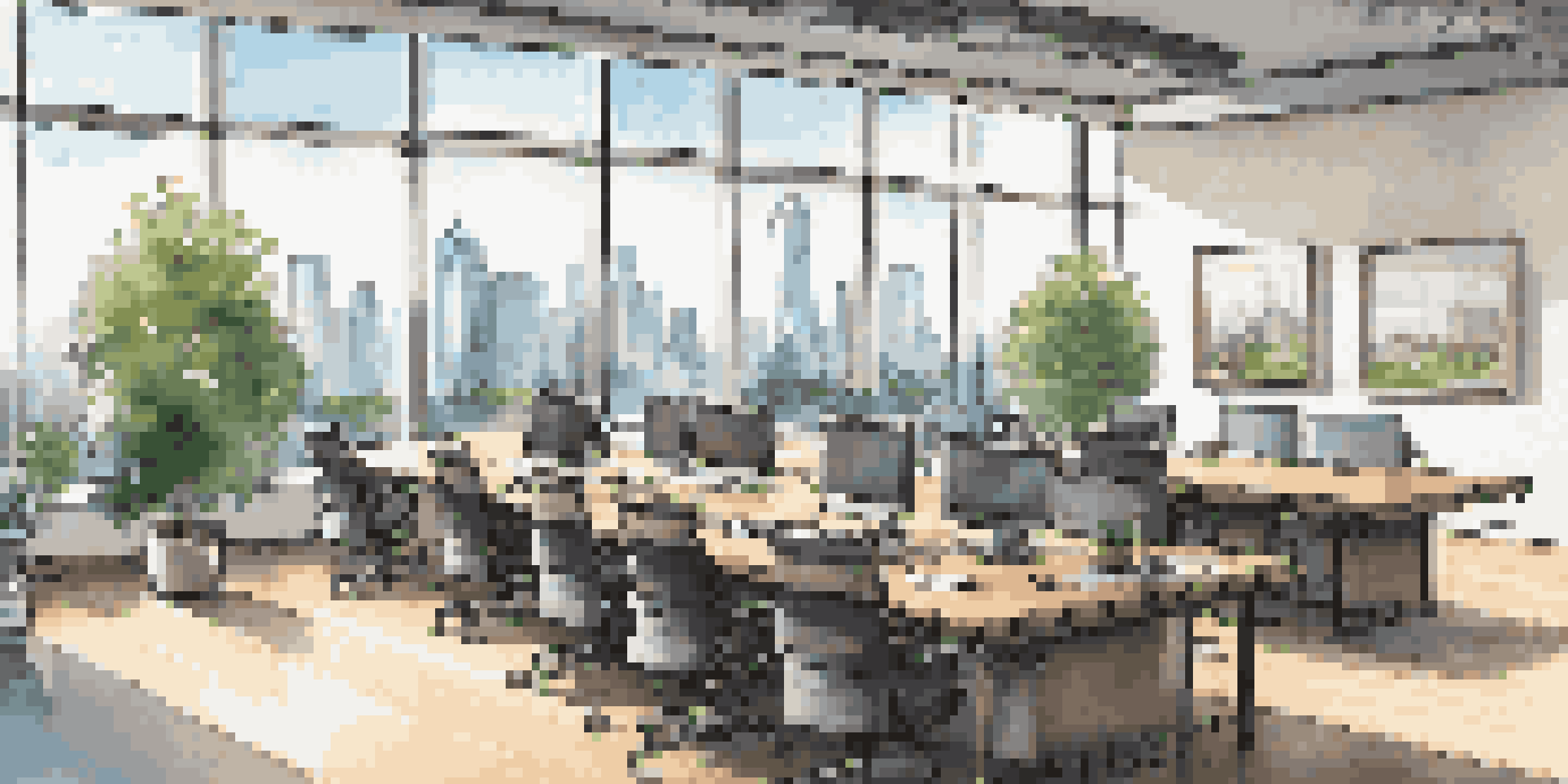 A bright modern office conference room with a wooden table, chairs, and a city skyline view through large windows.