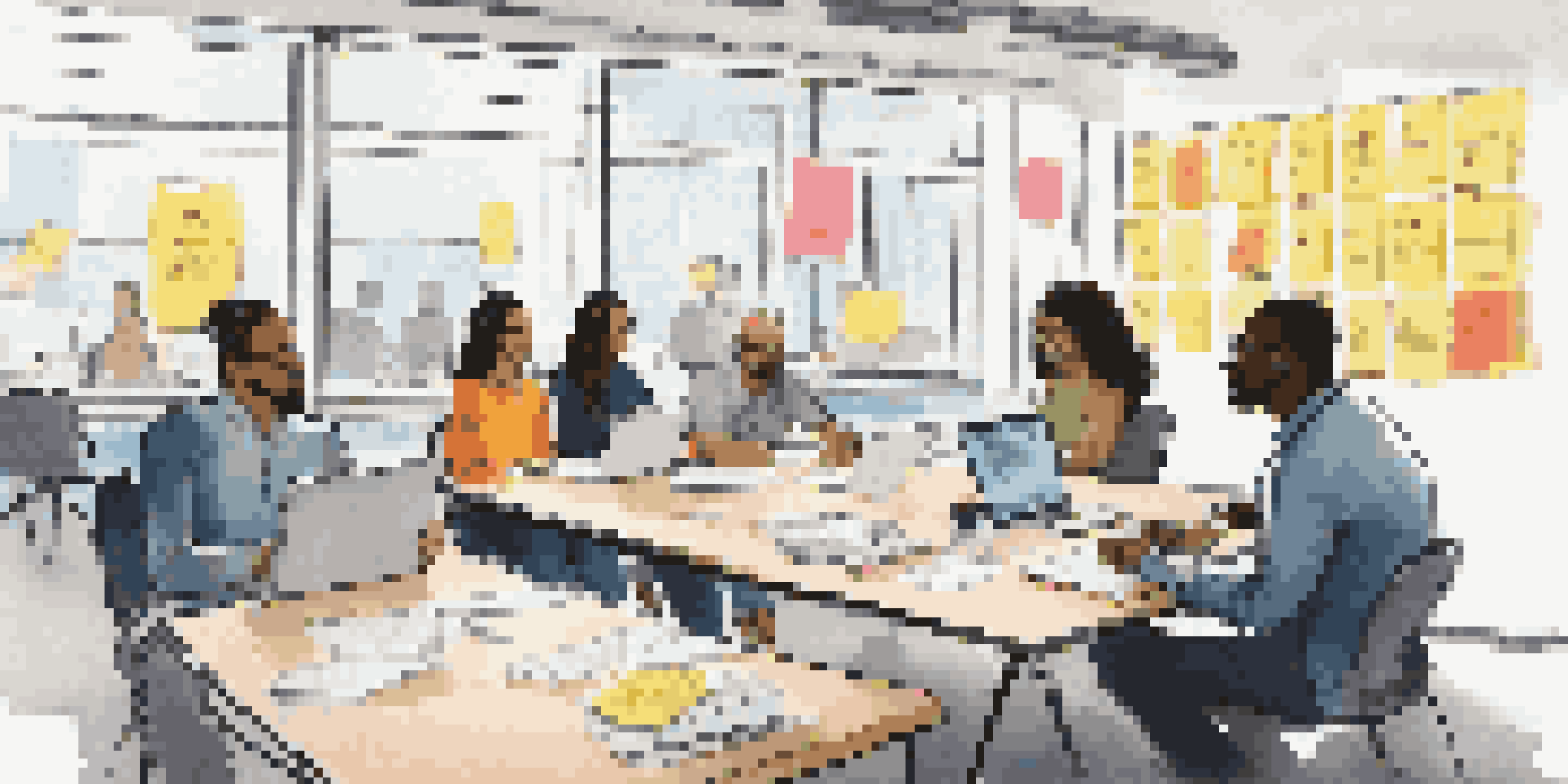 A diverse group of employees in a meeting, actively discussing and sharing ideas around a table filled with laptops and notepads.