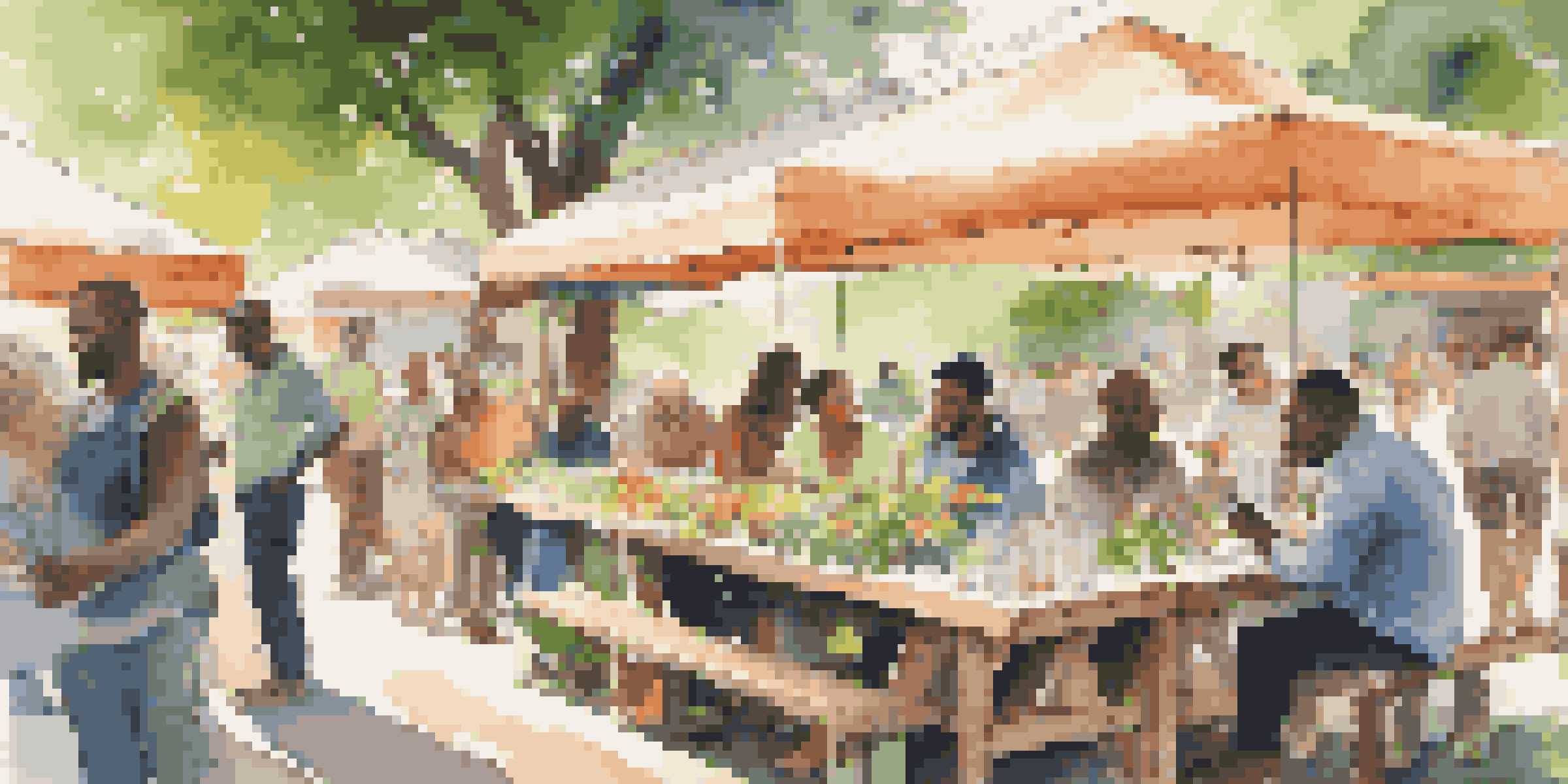 A diverse group of individuals discussing market research at an outdoor table with data charts and laptops, surrounded by greenery and flowers.