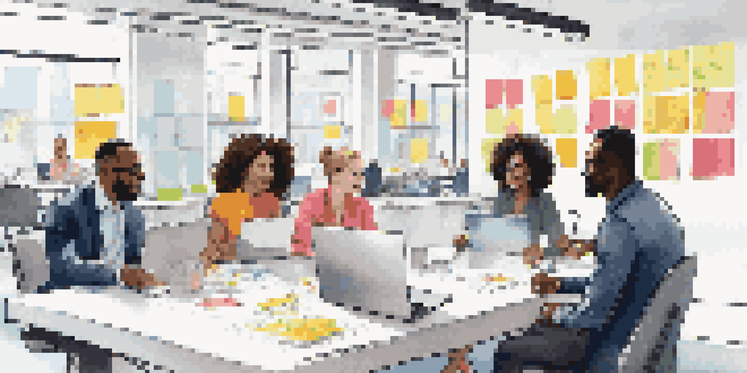 A diverse group of professionals engaged in a brainstorming session in a modern office with colorful sticky notes and laptops.