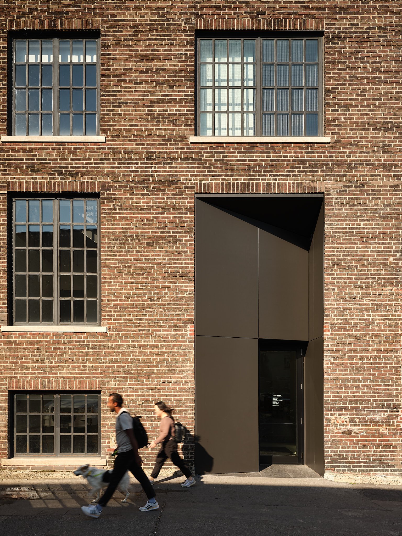 Two people walk past a brick warehouse entry