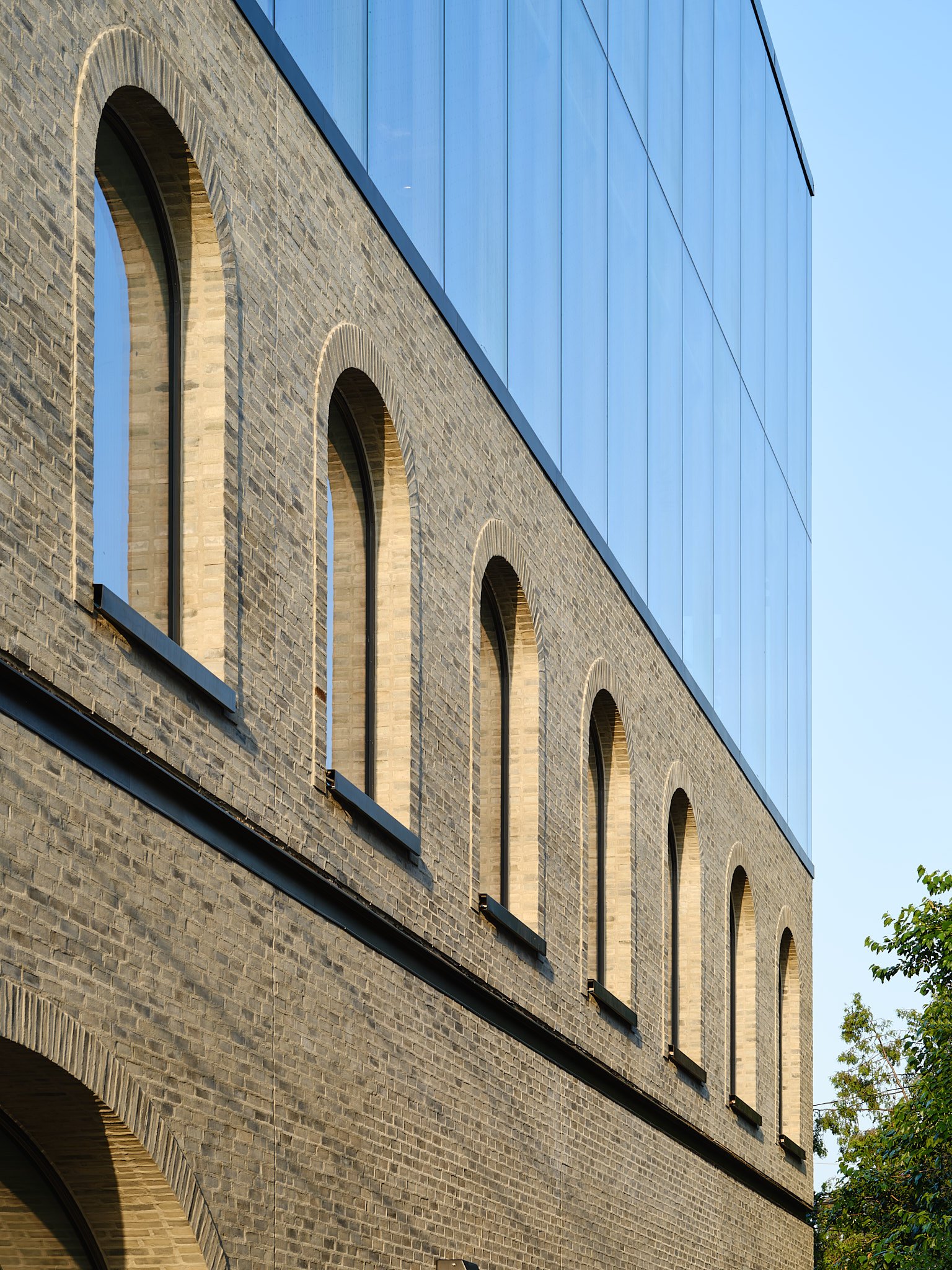 Glass addition above an arched brick facade