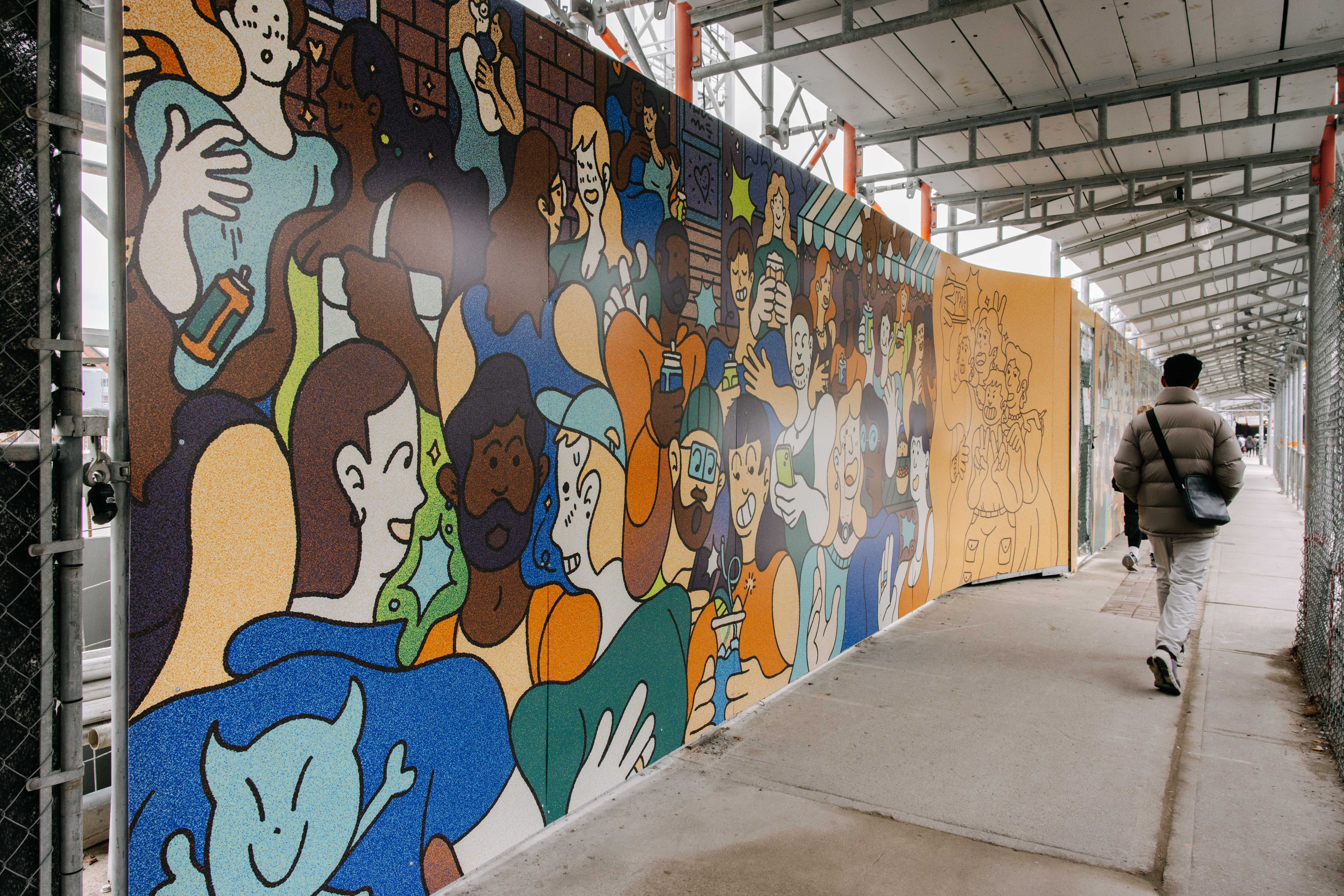 A person walks past a mural on a hoarding