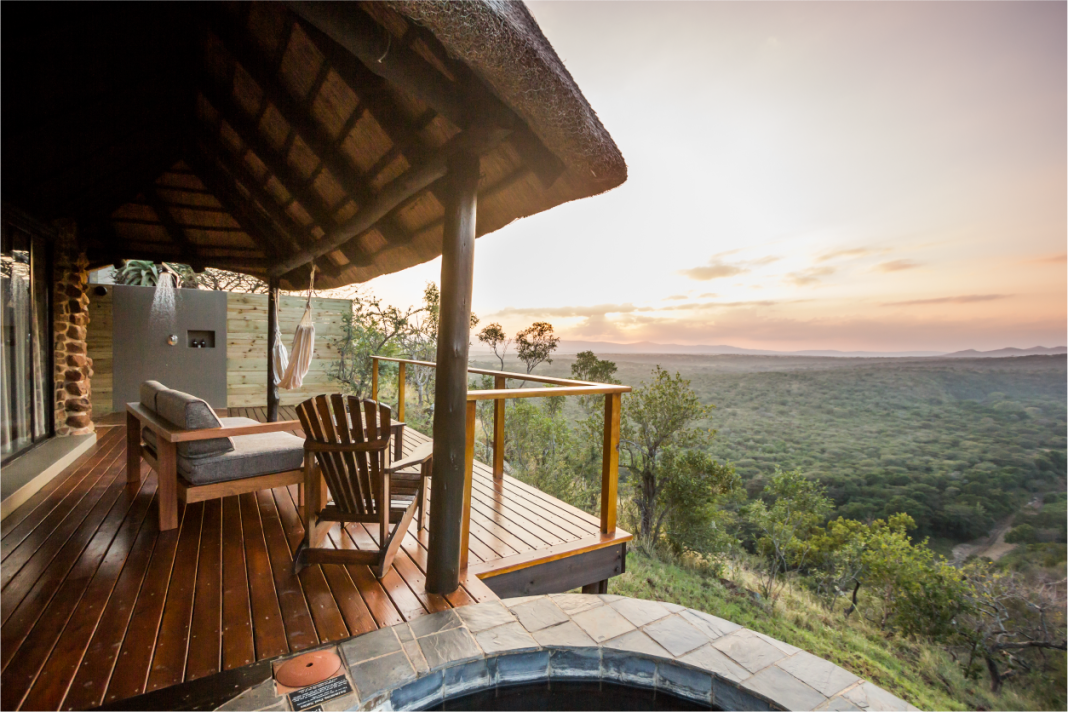 A suite deck with a wooden chair, hammock, outdoor shower and plunge pool overlooks the bushveld at dusk.