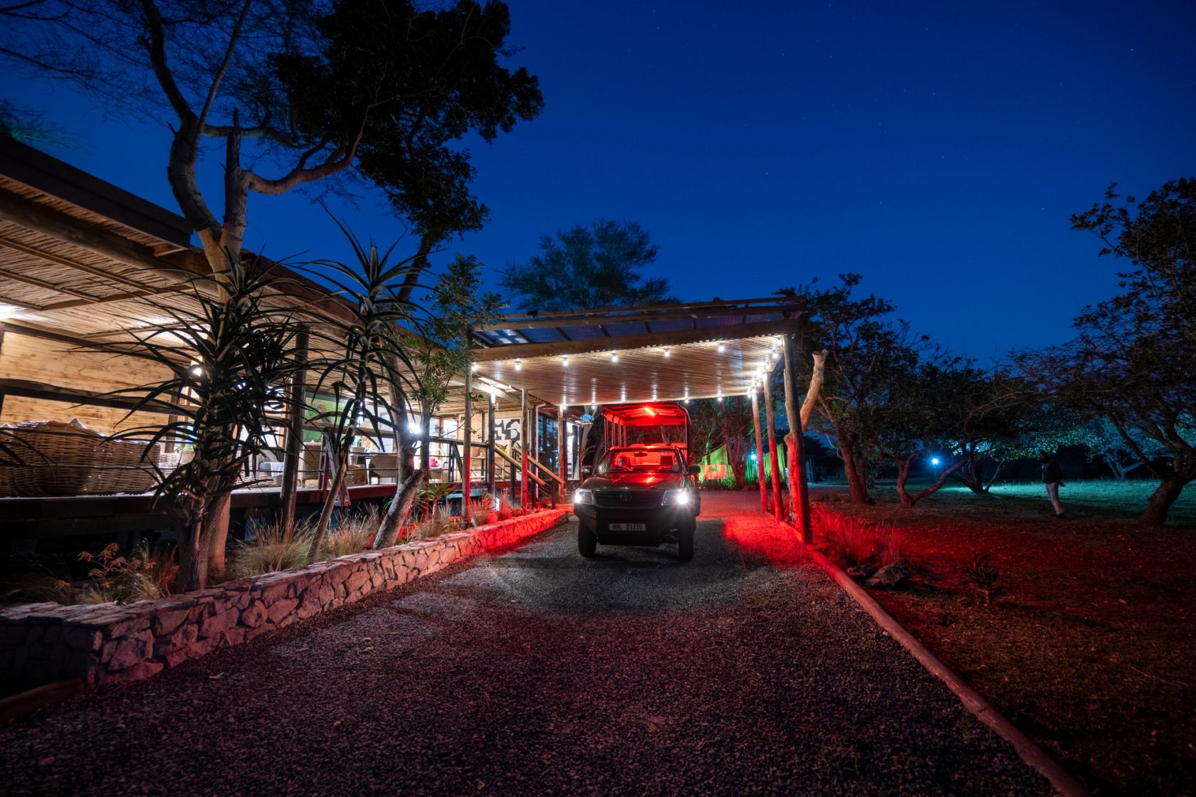 The lodge entrance at night, a game-drive vehicle arriving under the stars with the deck lit behind.
