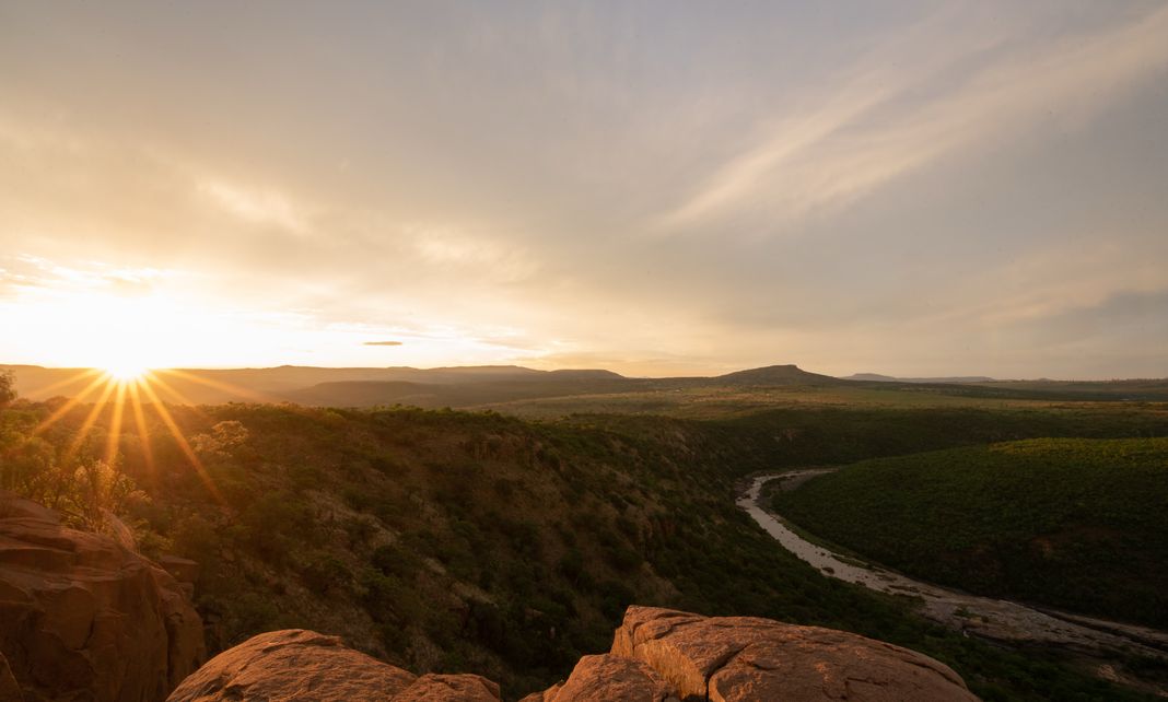 The sun sets over the Buffalo River gorge, with the river winding between wooded hills.