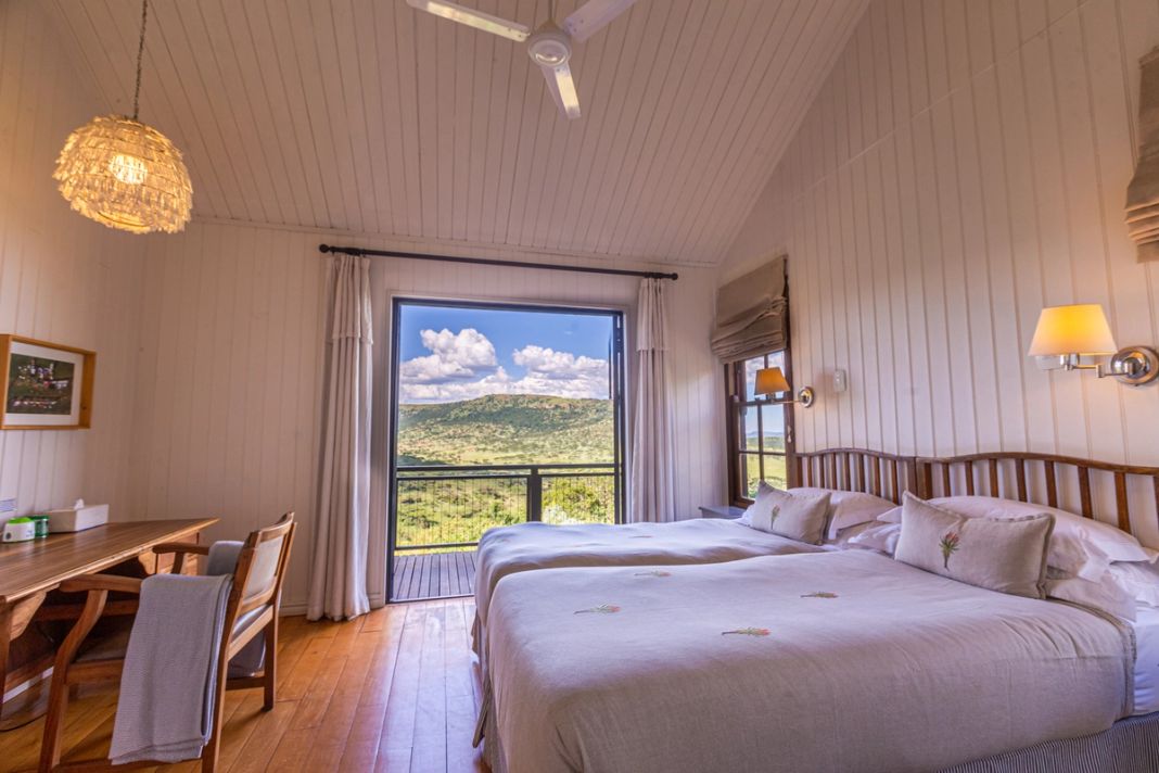 A twin bedroom with white linen and a sliding door opening onto a deck above a green valley.