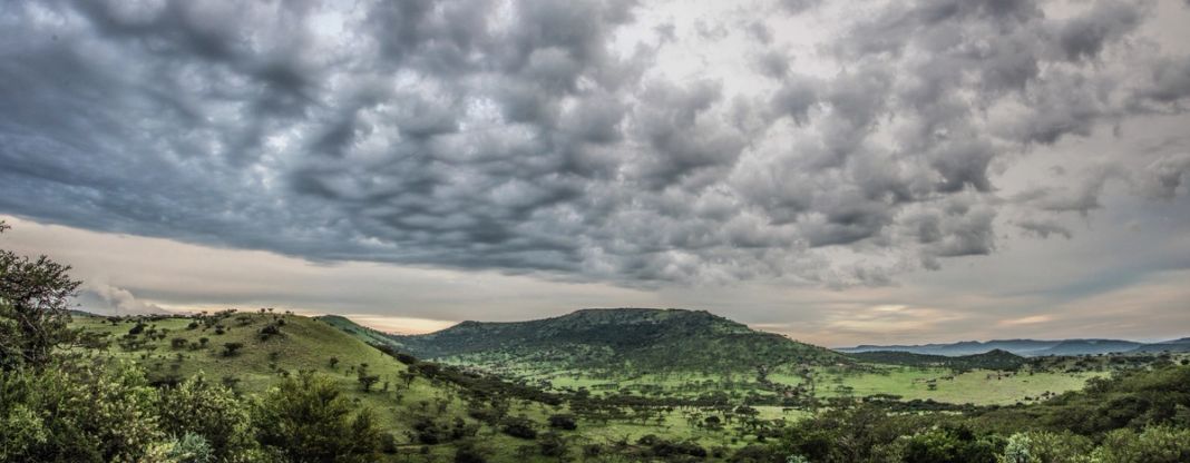 A wide view over green rolling farmland toward a flat-topped hill, under a heavy grey cloudscape.
