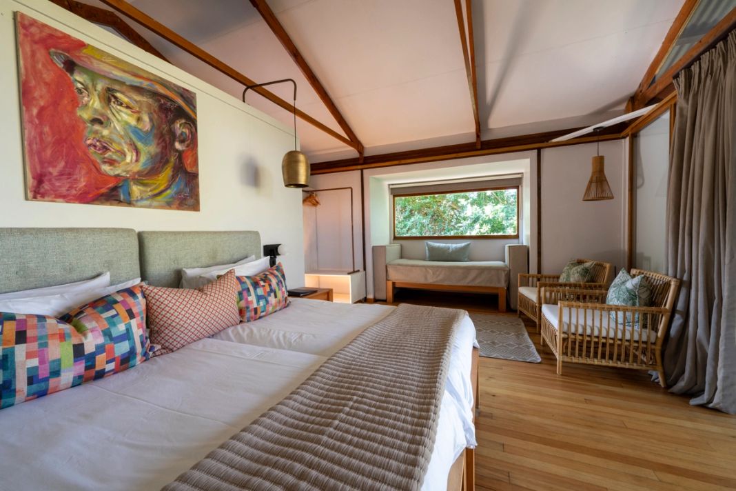 A suite bedroom with a portrait painting above the bed, a window seat, and cane chairs on the timber floor.