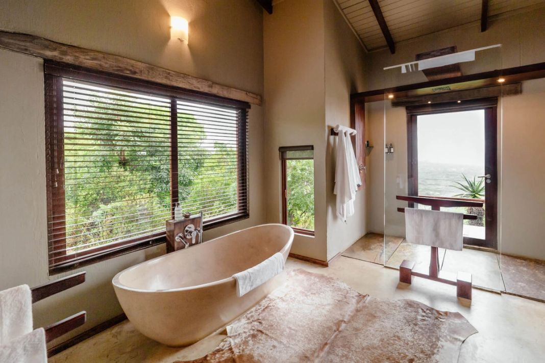 A honeymoon villa bathroom with a freestanding stone tub, blind-covered windows and a cowhide rug.