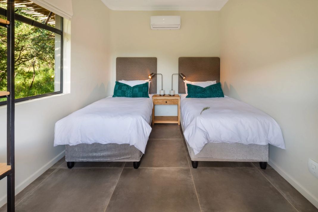 A compact room with two single beds, green cushions and a window onto foliage, set as a second sleeping area.