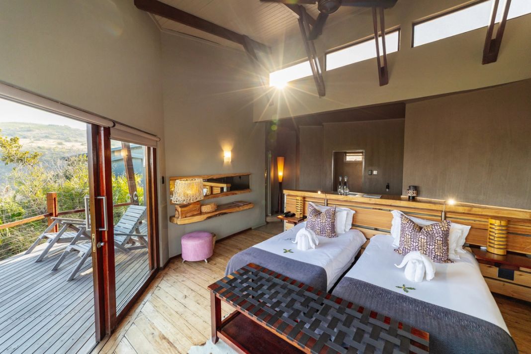 A family room with two single beds against a live-edge headboard and glass doors to a view deck.