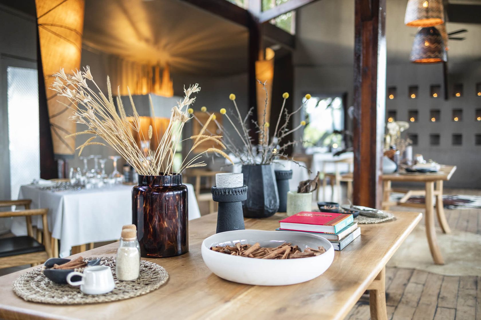A dining table is styled with dried grasses, an amber jar and a white bowl of cinnamon sticks in the restaurant.