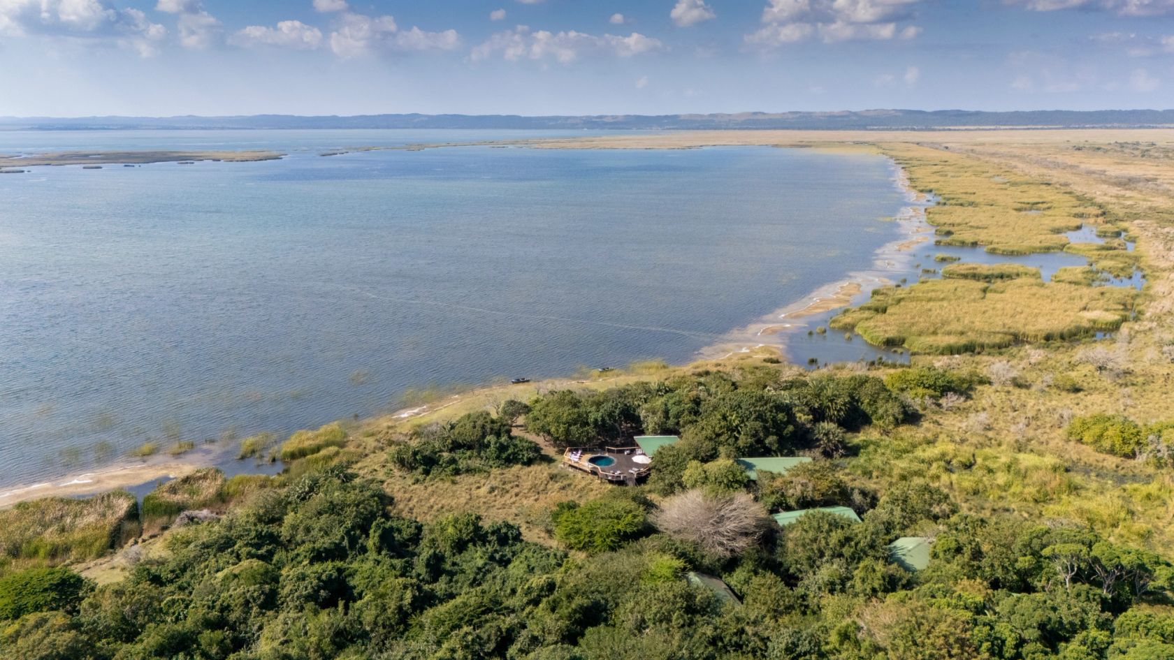 Wide daytime aerial of the lodge hidden in dune forest where the wetland shoreline meets Lake St Lucia.