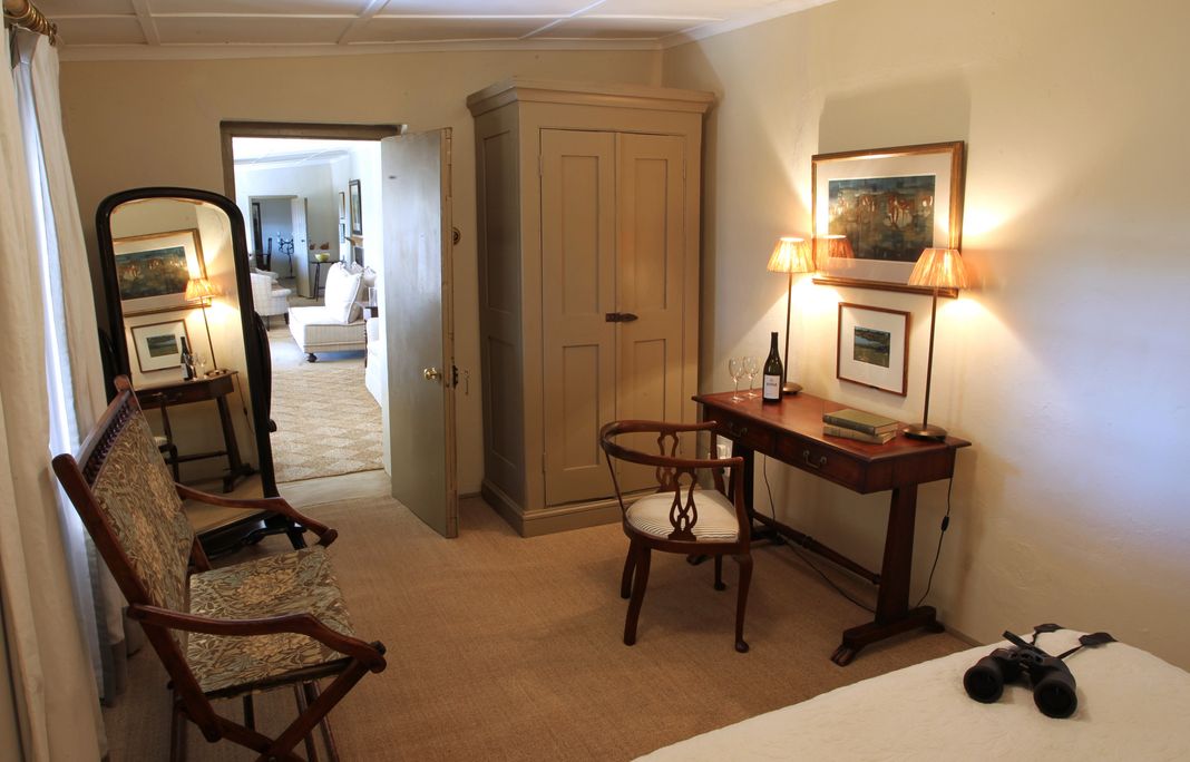 An Umzinyathi bedroom with an antique wardrobe, a writing desk, a mirror and binoculars resting on the bed.