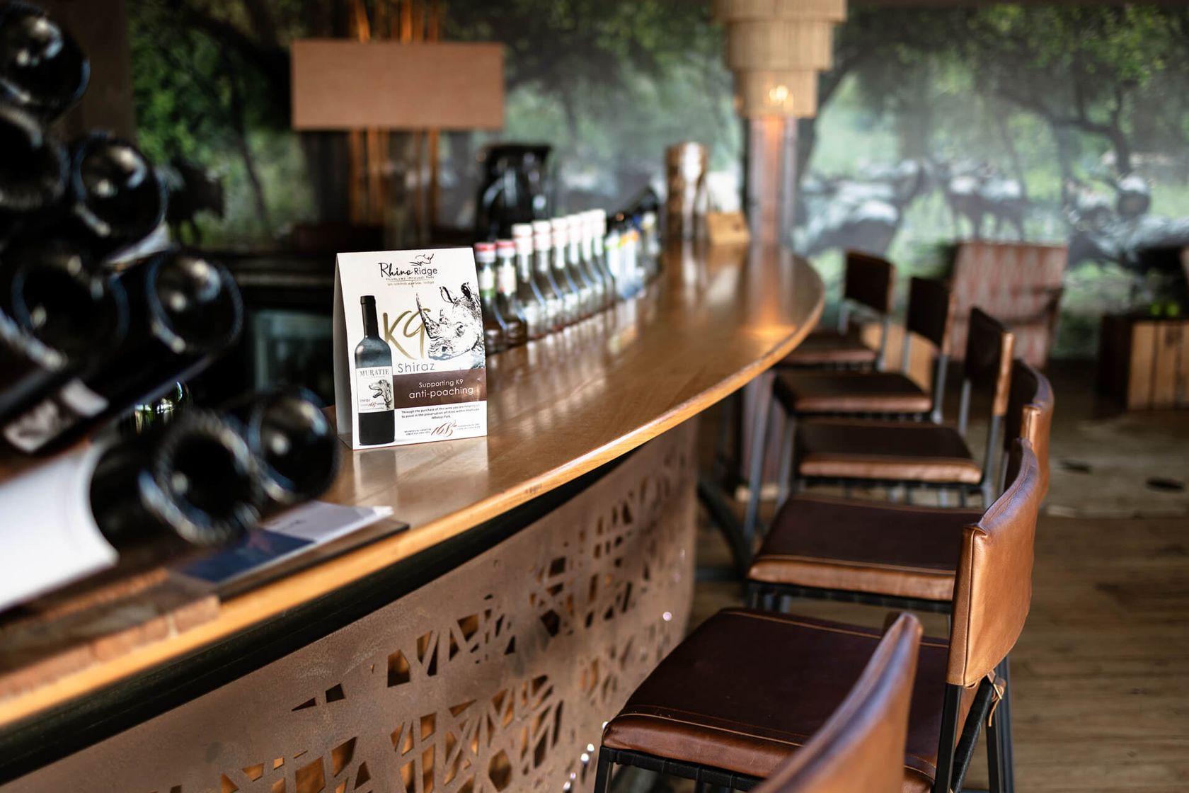 A wine card supporting K9 anti-poaching stands on the curved bar counter beside leather stools.