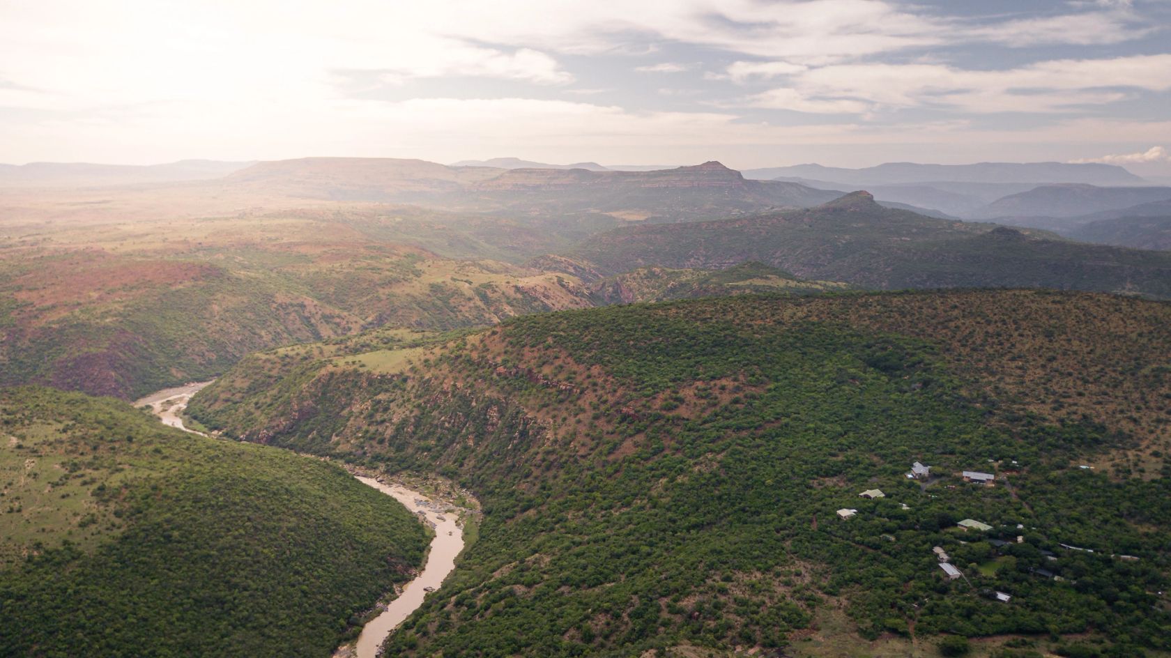 An aerial view of the Buffalo River winding through a green gorge, with the lodge set among trees on the right.