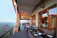 A long dining table set on a covered veranda with kudu horns on the wall, overlooking the gorge at dusk.