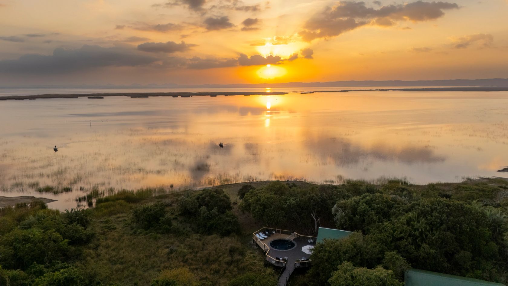 The sun sets over Lake St Lucia, with the lodge pool deck at the forest edge below.