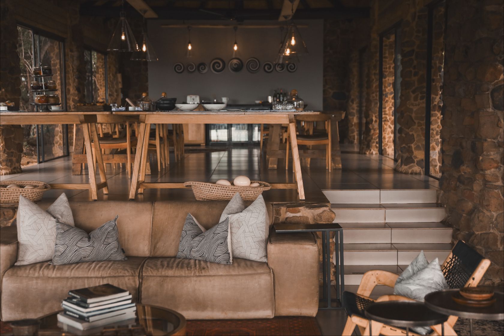 A trestle dining table and low leather sofa in a stone-walled open-plan lodge interior.