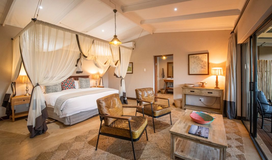 A lodge room with a four-poster bed under draped netting, leather armchairs and a framed map on the wall.