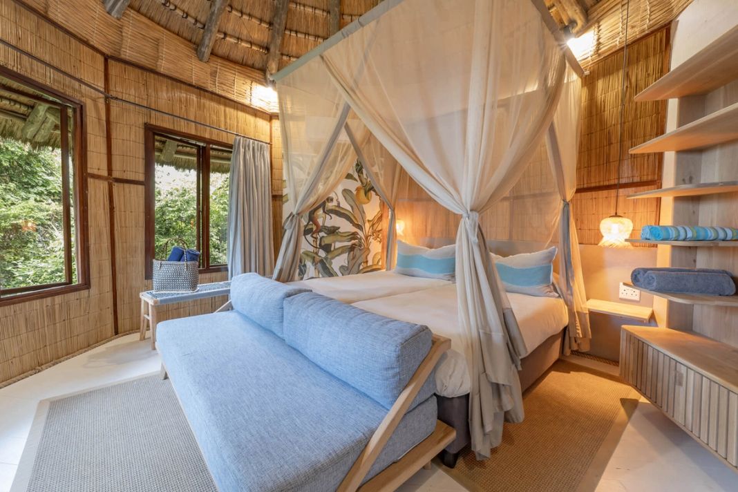 A reed-walled room with a king four-poster, a blue daybed and shelves of rolled towels.