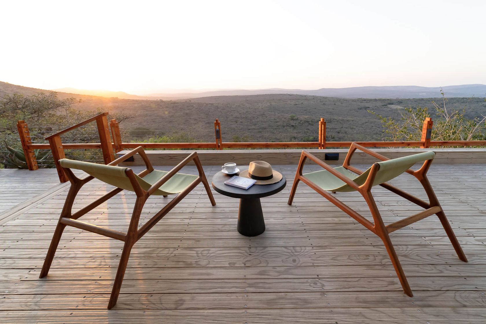 Two sling chairs face the bushveld from the deck at sunset, with coffee, a hat and a book on the side table.