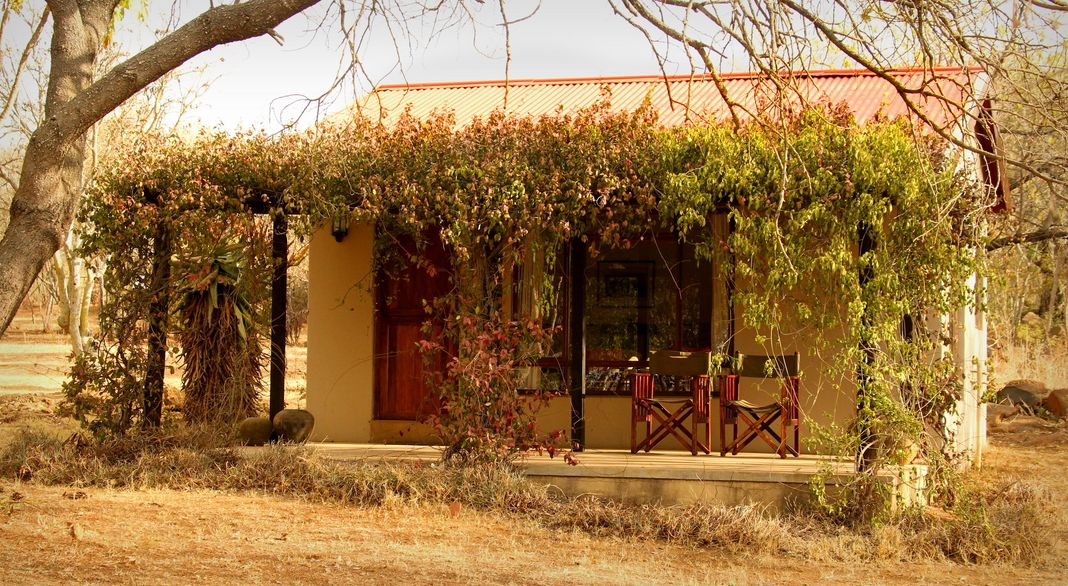 The Umzinyathi stone farmhouse with a red corrugated roof and a vine-covered veranda set among dry bushveld.