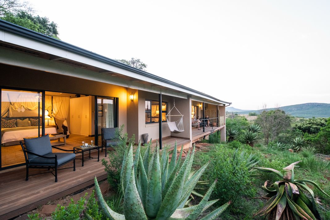 The lodge room wing at dusk, its verandas lit from within, with an aloe in the foreground and the plains behind.