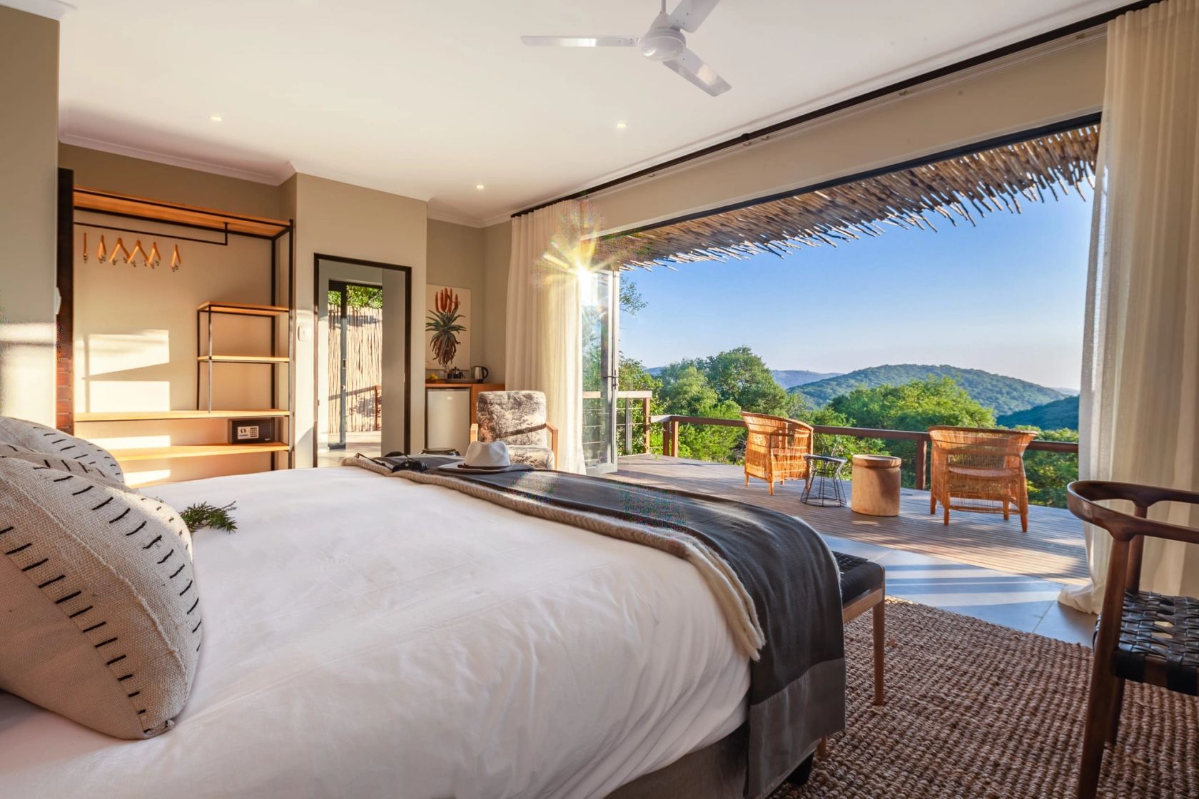 A suite with a white-linen bed and open stack-back doors leading to a deck overlooking forested hills.