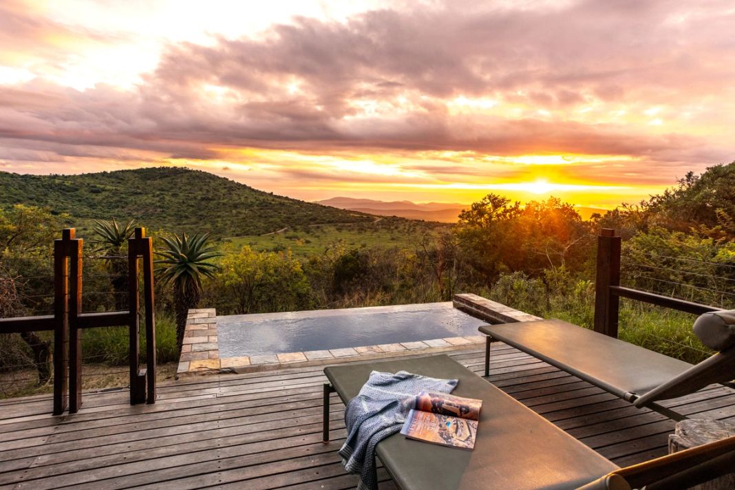 Private deck with a plunge pool and a towel-draped lounger, facing the hills under a sunset sky.