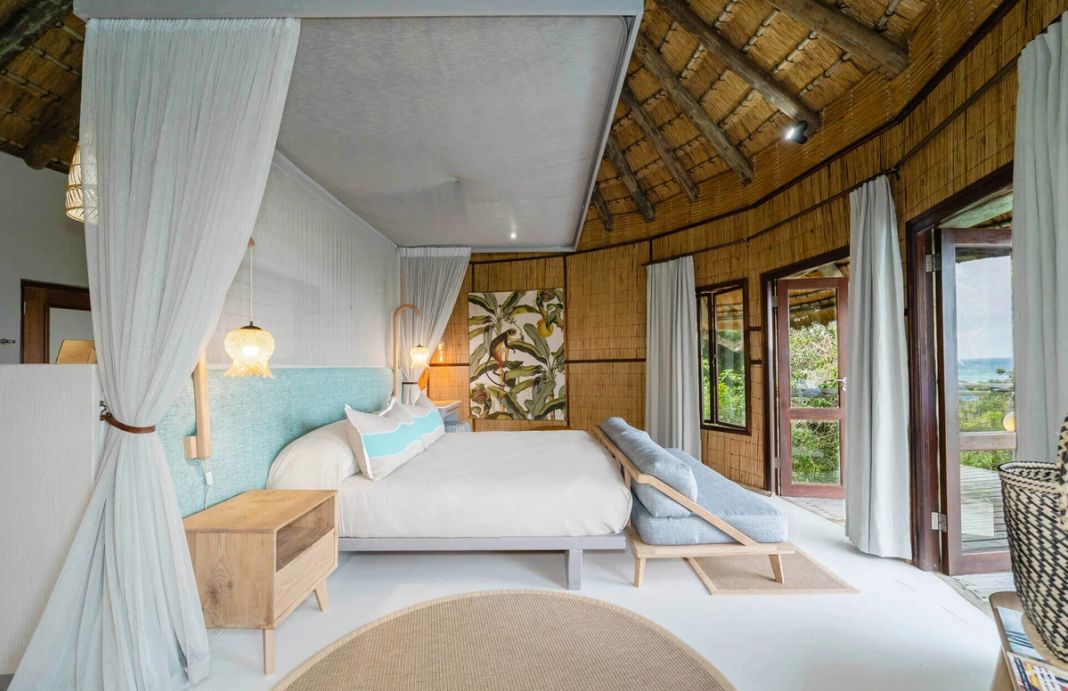 A king room with a turquoise headboard and glass doors opening to a deck with the ocean beyond.