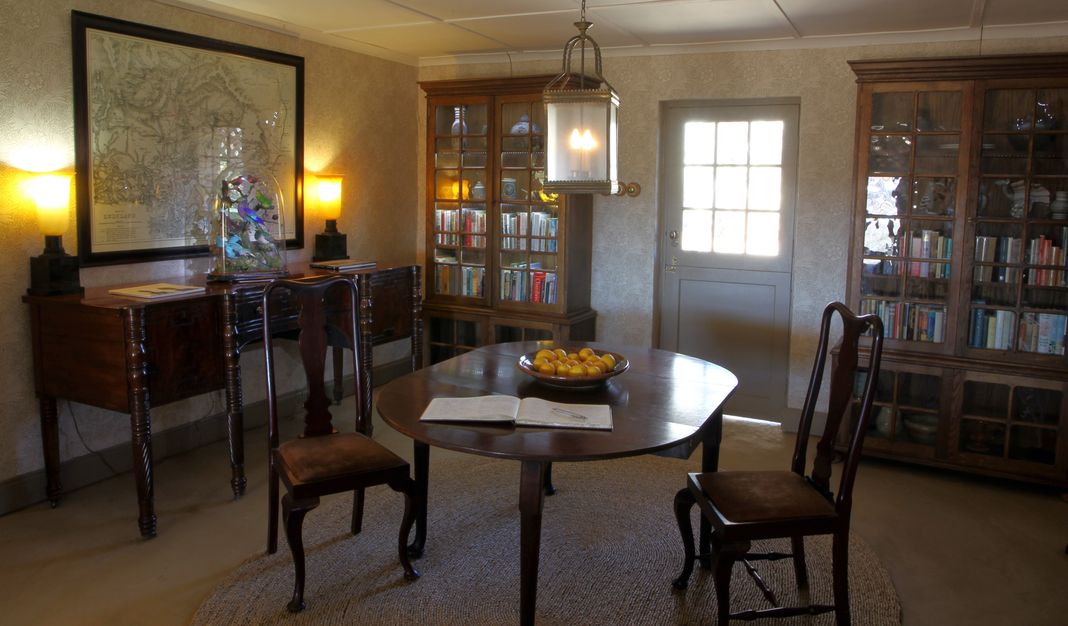 Interior of the Umzinyathi farmhouse with a framed antique map, glass-front bookcases, and a round table set with a bowl of lemons.